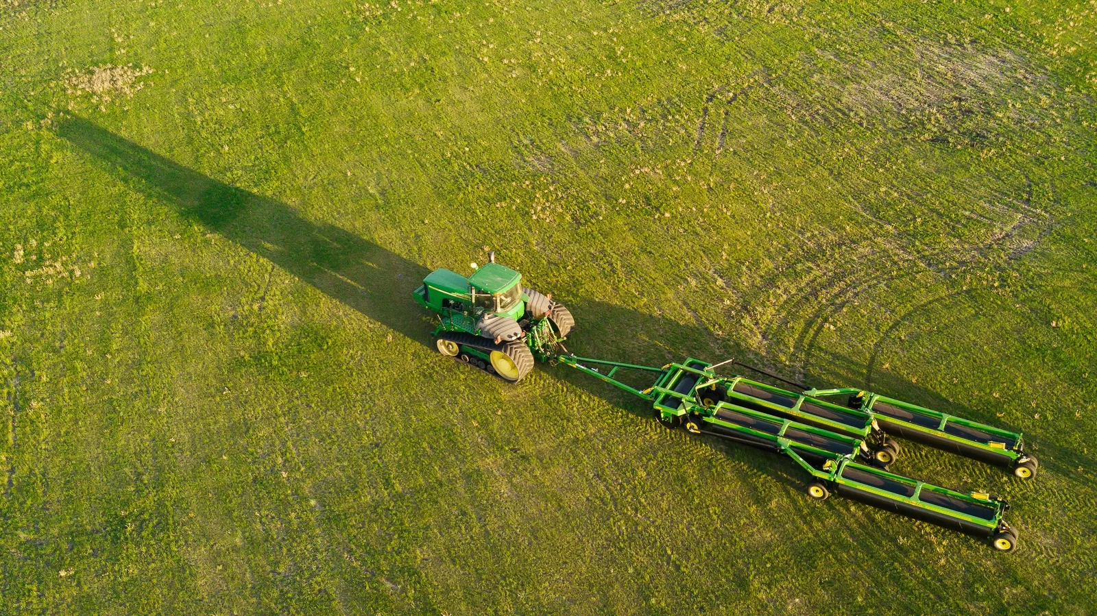 Aerial view of green tractor pulling Mandako 5 PLEX LANDROLLER across sprouting crop field