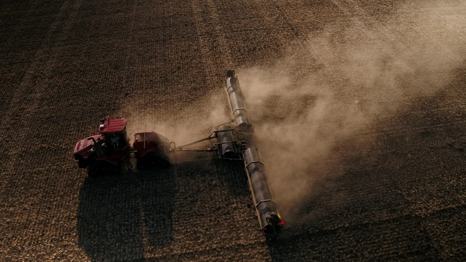 Aerial view of red tractor and combine harvester creating dust clouds while harvesting dry grain crop