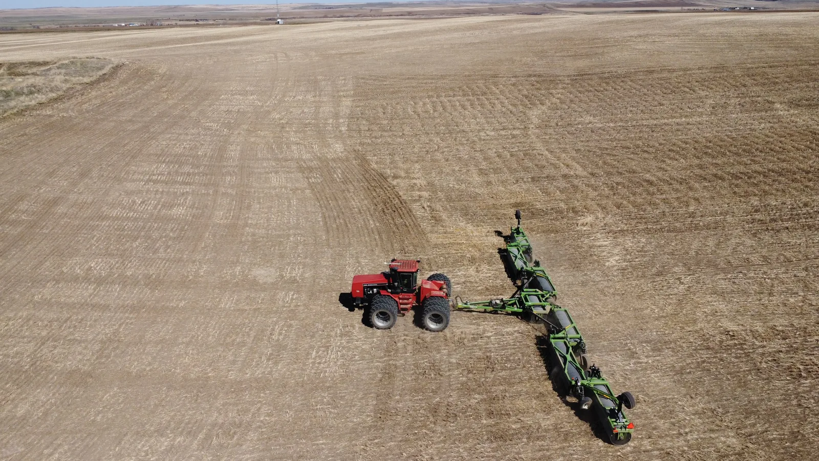 Aerial view of red tractor with green land roller working across stubble field