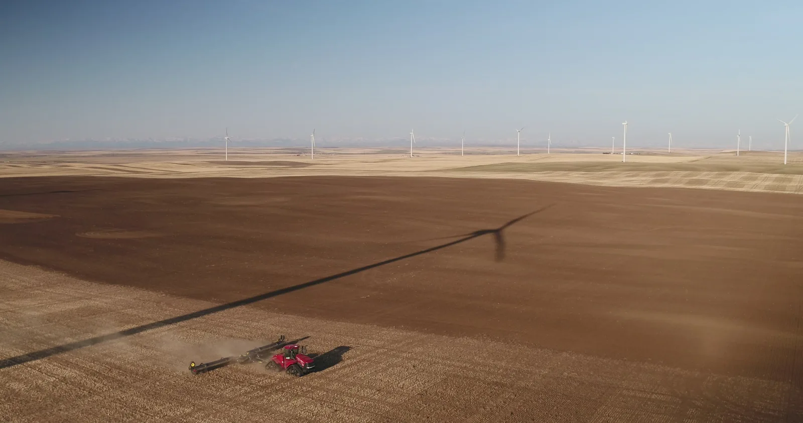 Aerial view of worked brown soil field with wind turbines on horizon