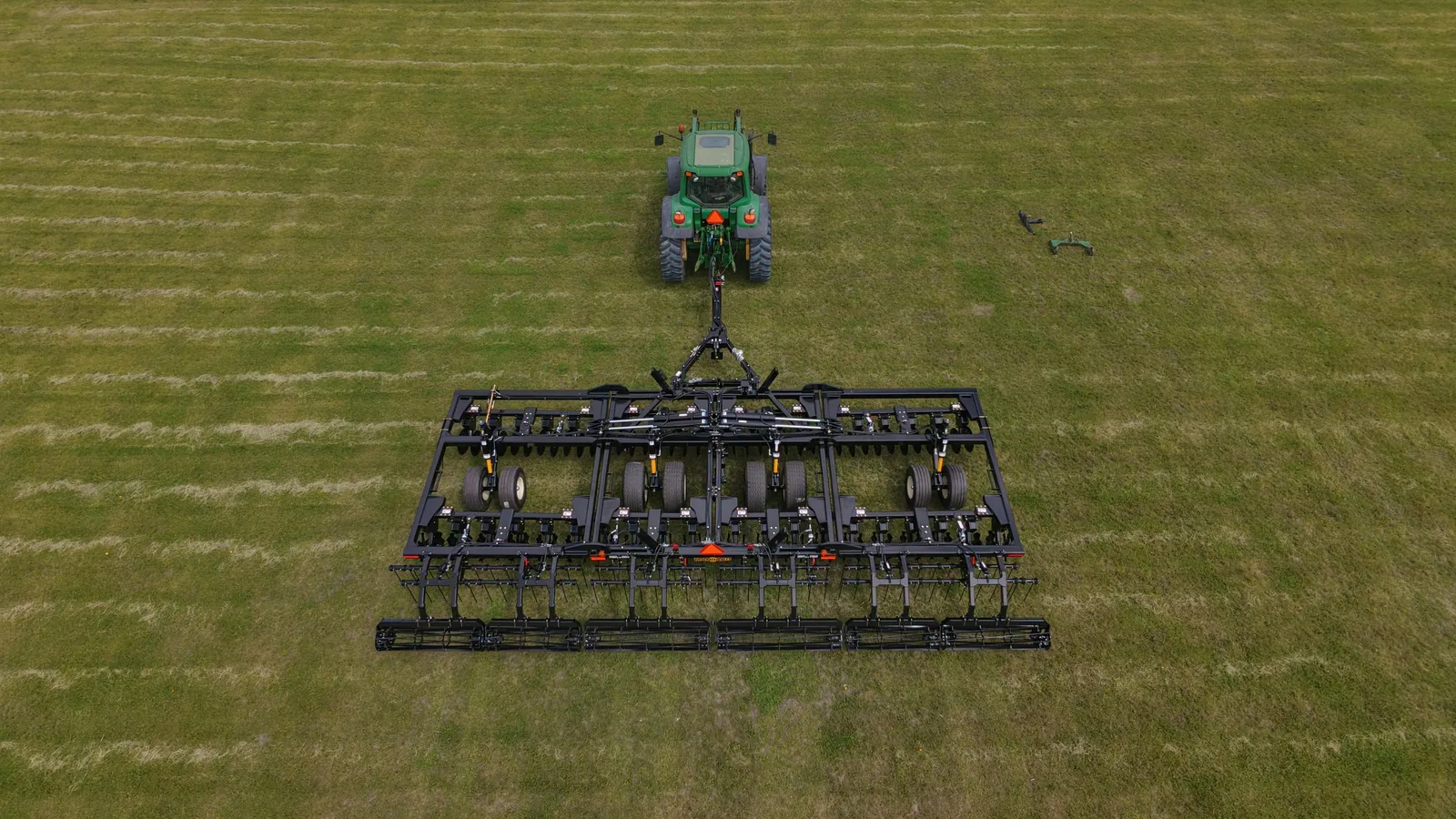 Green tractor pulling Mandako Storm vertical tillage implement across grass field