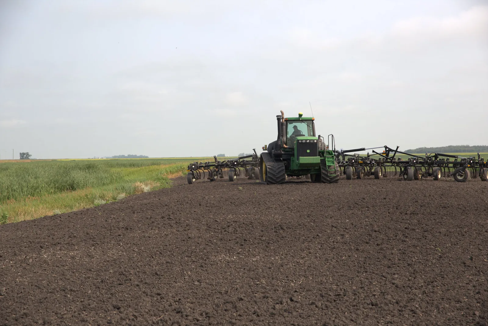 Green tractor with Mandako Chisel Flex working dark soil in spring field