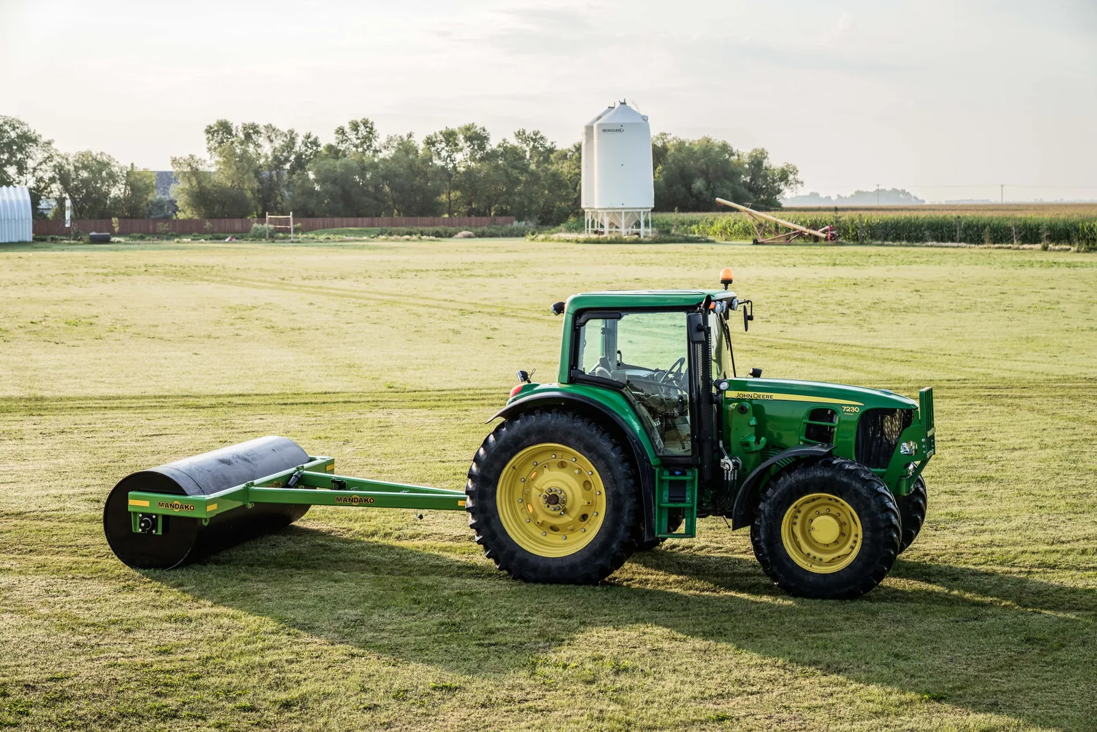Green tractor with Mandako Single Landroller in field near farm buildings
