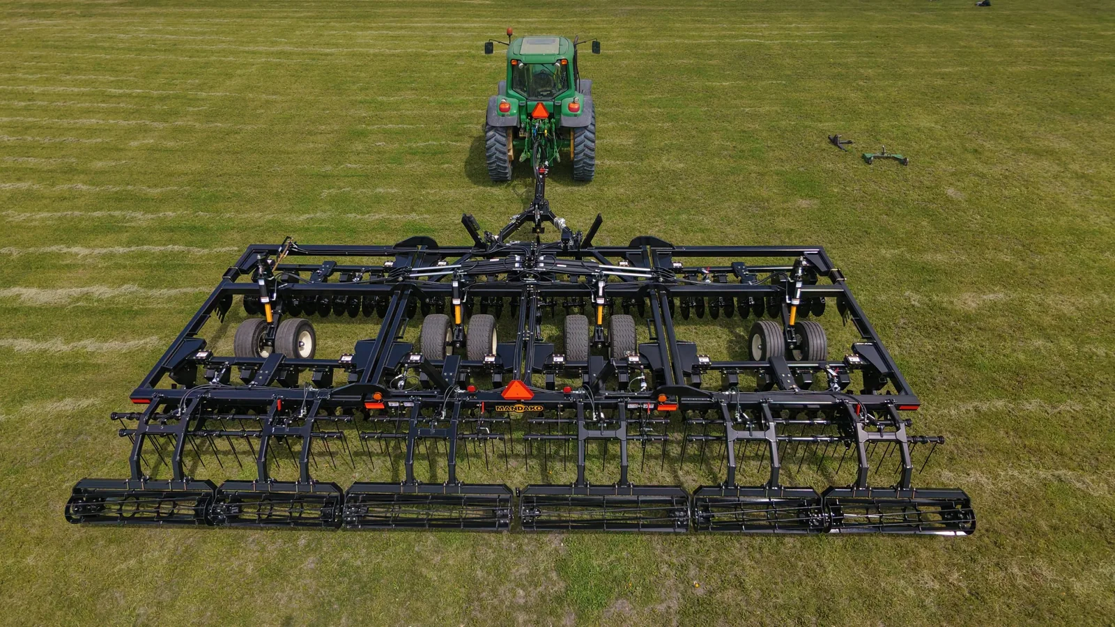 Green tractor with Mandako Storm vertical tillage implement working in field, aerial view