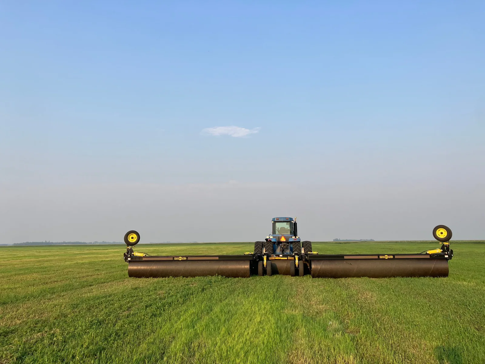 Land roller with yellow gauge wheels working through green spring crop field