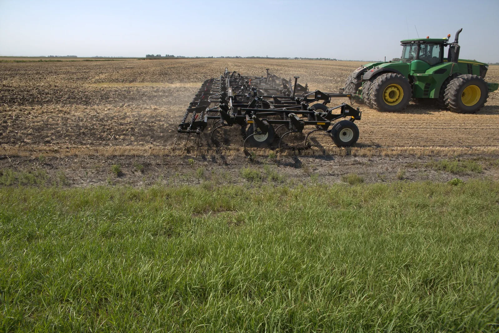 Mandako Chisel Flex pulled by green tractor across black soil field with green cereal crop in foreground