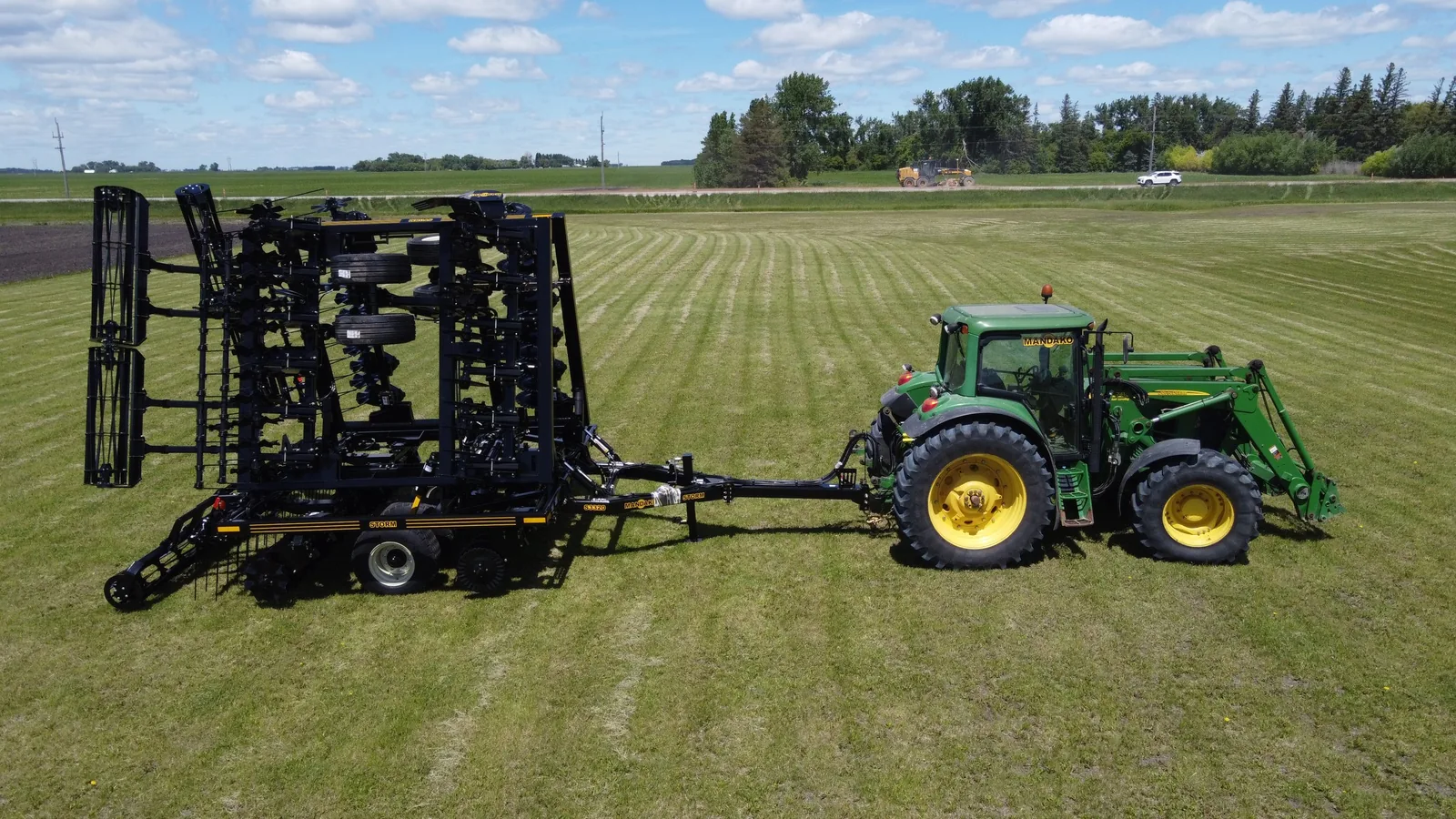 Mandako Storm pulled by green tractor in open field with striped crop rows
