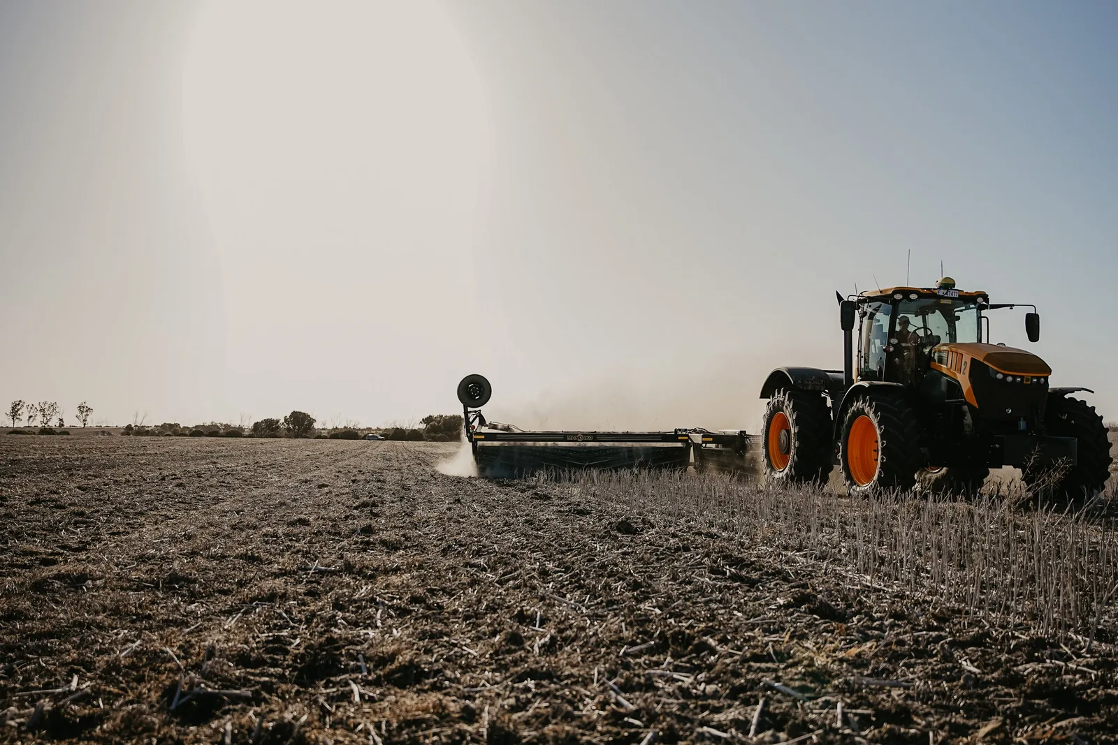 Orange and black tractor pulling Mandako Cover Crop Crimper across stubble field
