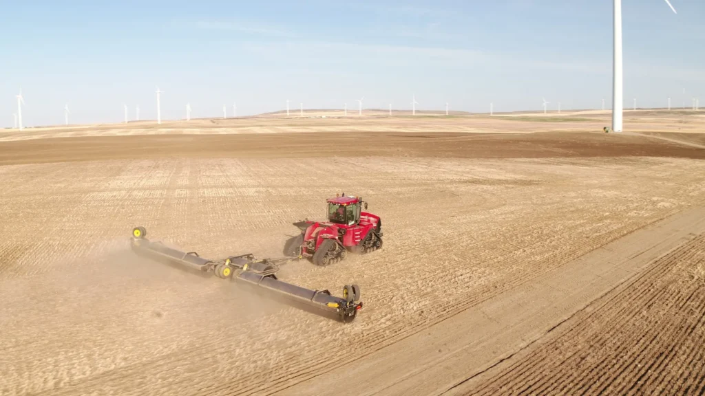 Red tractor with Mandako 3 PLEX LANDROLLER creating dust clouds while rolling spring soil | Mandako Red tractor with Mandako 3 PLEX LANDROLLER creating dust clouds while rolling spring soil