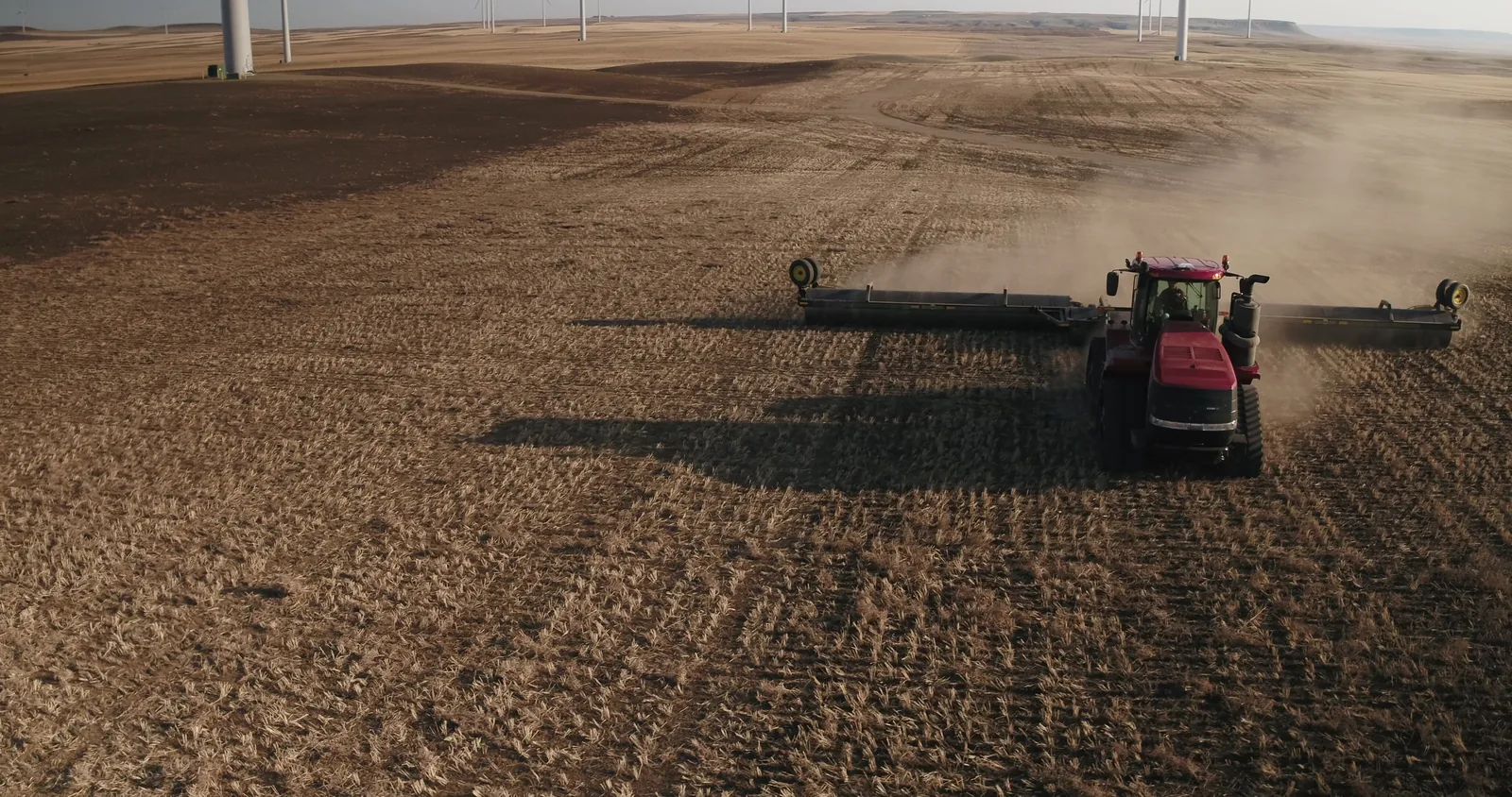 Red tractor with Mandako land roller creating dust cloud while working across stubble field