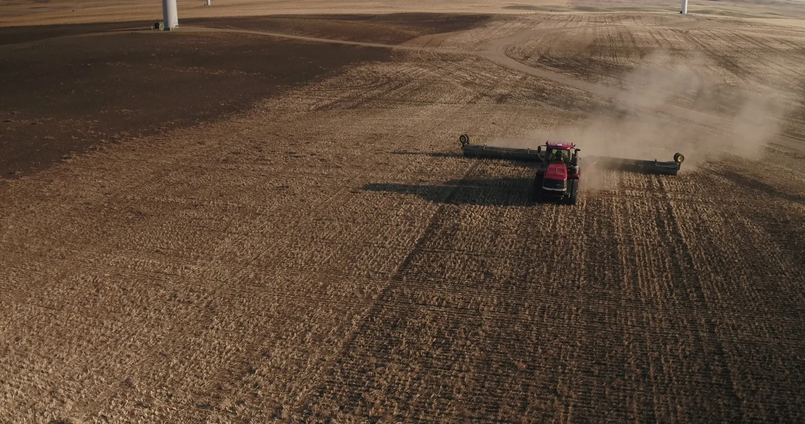 Red tractor with wide tillage implement working dusty stubble field in fall