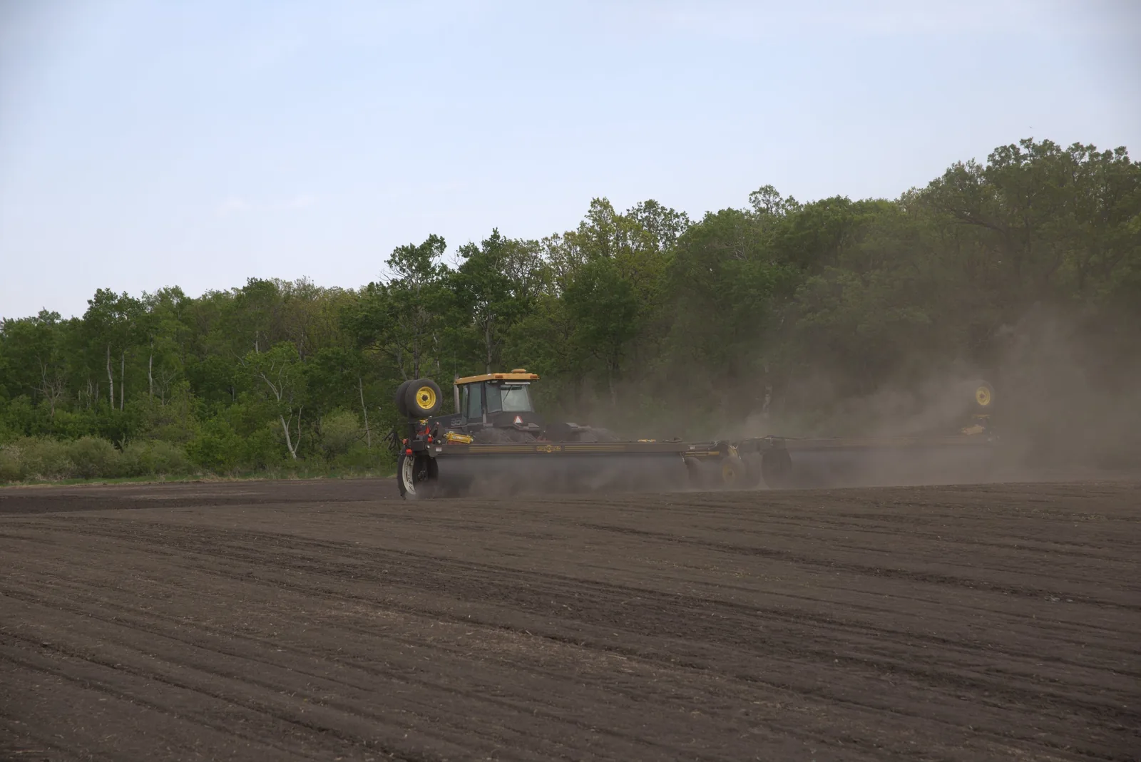 Yellow tractor with Mandako 3 PLEX LANDROLLER creating dust clouds across bare field